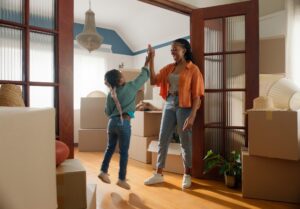 A woman and her young daughter in a room cluttered with boxes, both excited about their new space.