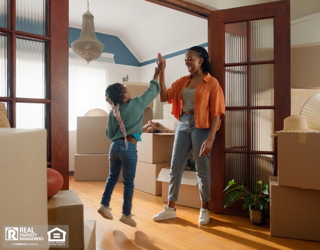 A woman and her young daughter in a room cluttered with boxes, both excited about their new space.