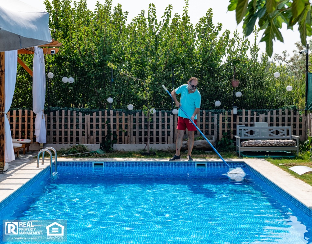 A man in flip flops cleaning a swimming pool with a net.