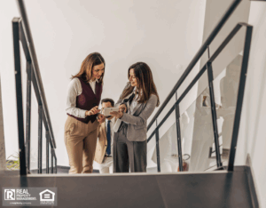 Two businesswomen on stairs in an office building, discussing plans for a rental property.
