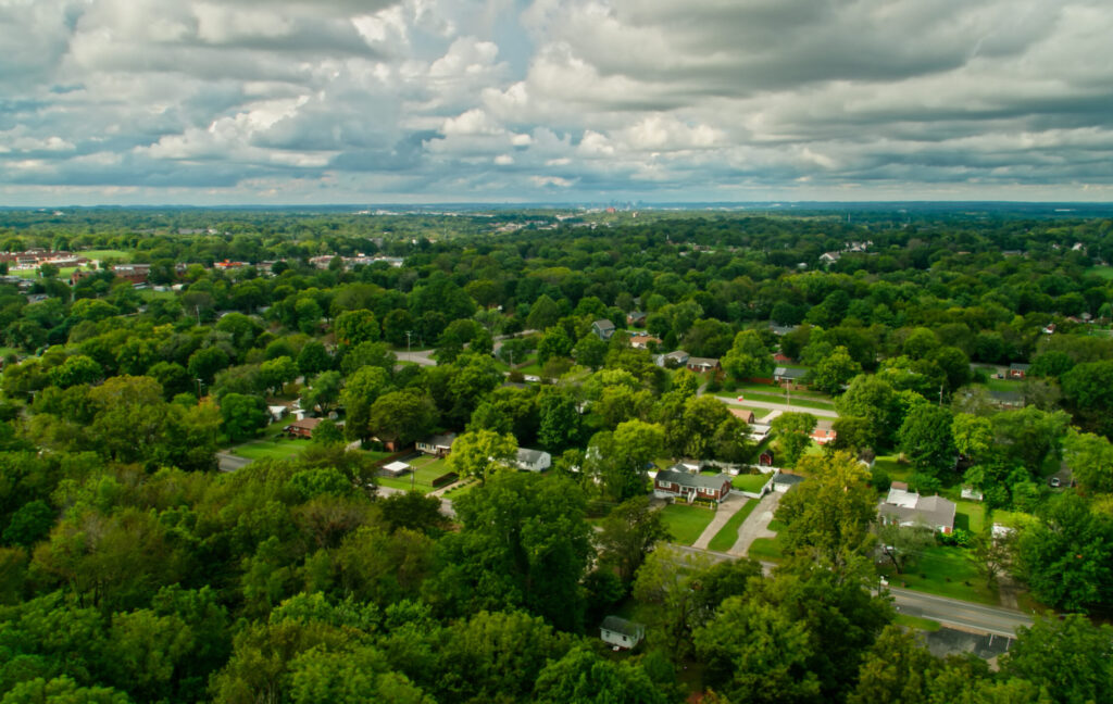 Aerial shot of a residential neighborhood in the southern suburbs of Nashville, Tennessee, with a view across the thickly wooded rolling landscape towards the downtown skyline in the distance.  

Authorization was obtained from the FAA for this operation in restricted airspace.