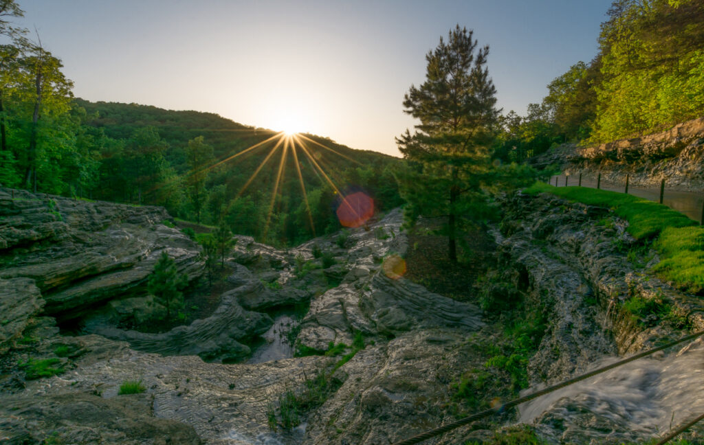 Rocky waterfall overlook at sunset in the Ozark Mountains, Missouri and Arkansas.  Green summer foliage and sunburst.
