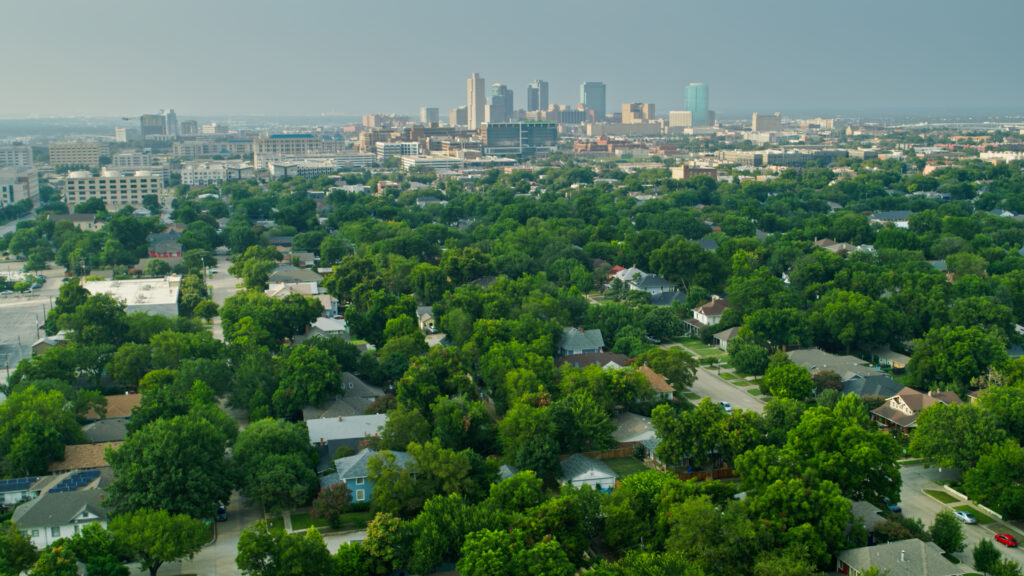 Aerial shot of of suburban streets in Fort Worth, Texas on a sunny day in summer, with the downtown skyline in the distance.
