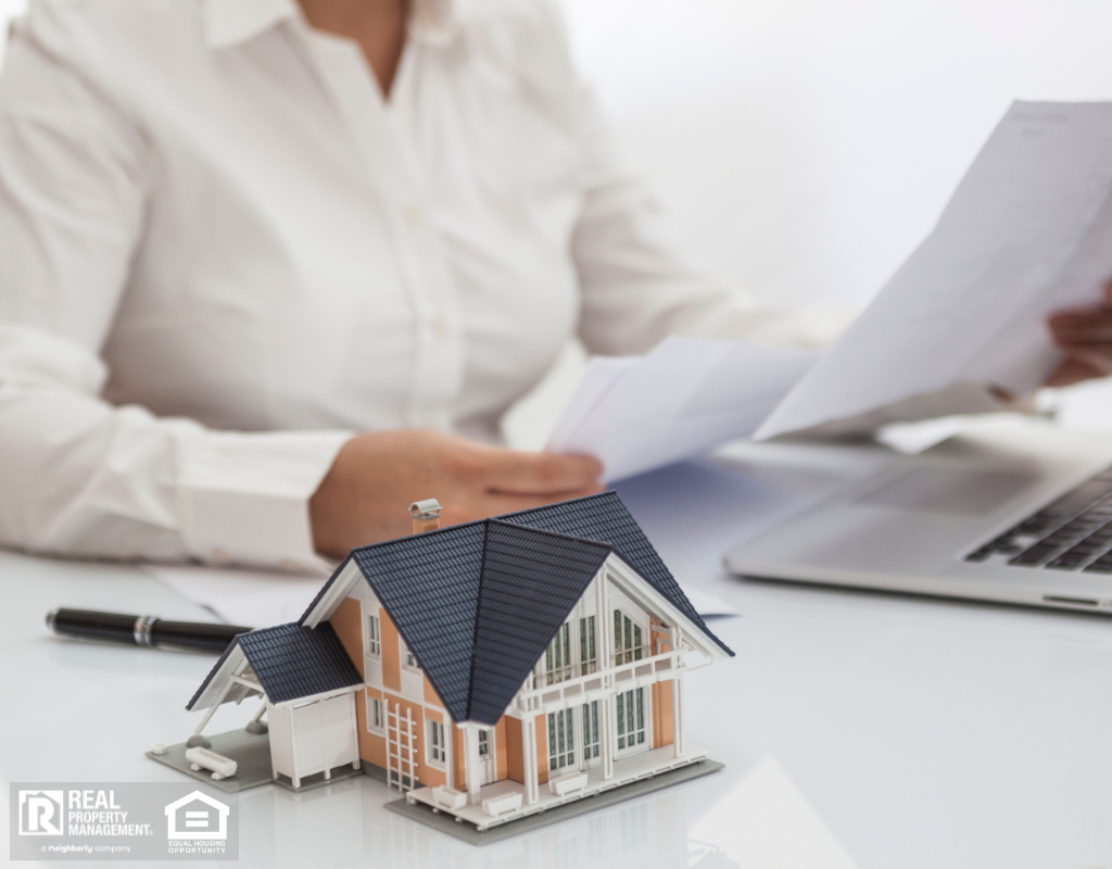 A woman working on a laptop at a desk with a house model, highlighting the advantages of real estate investment.