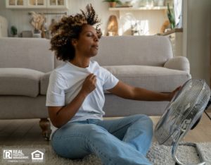A woman sits on the floor using a fan to cool off from the summer heat.