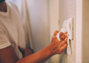 An individual using a cloth to wipe a light switch, highlighting the importance of cleanliness in everyday objects.