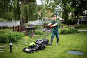 A man in overalls is actively mowing the lawn, surrounded by fresh greenery.