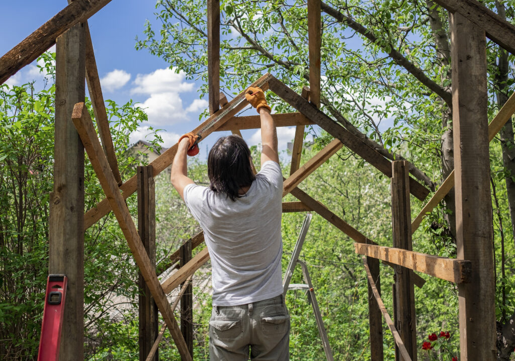 Man using tape measure while building a wooden structure.