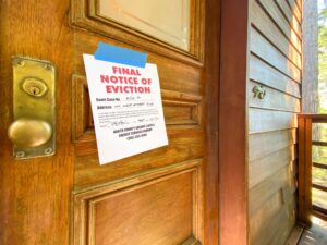 Eviction notice on door of house with brass door knob. Fictitious address, ID, signature and 555 phone number for fictional usage.