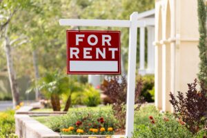 A for-rent sign is in the yard of a sunny home.