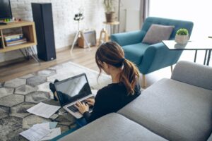 A woman at home sitting on the floor with a laptop, doing her financials.