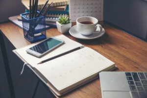A laptop, coffee cup, and notebook neatly arranged on a desk.