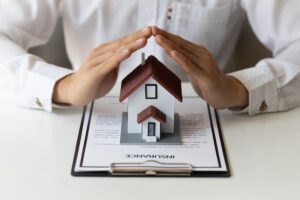 Man holds a house model above an insurance plan.