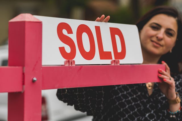 a-sold-sign-with-a-person-standing-in-the-background-slightly-out-of-focus.