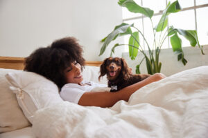 Young woman waking up in bed in the morning with her cute little dachshund.