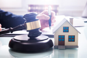 Gavel with sound block and house model over desk in front of a property manager.