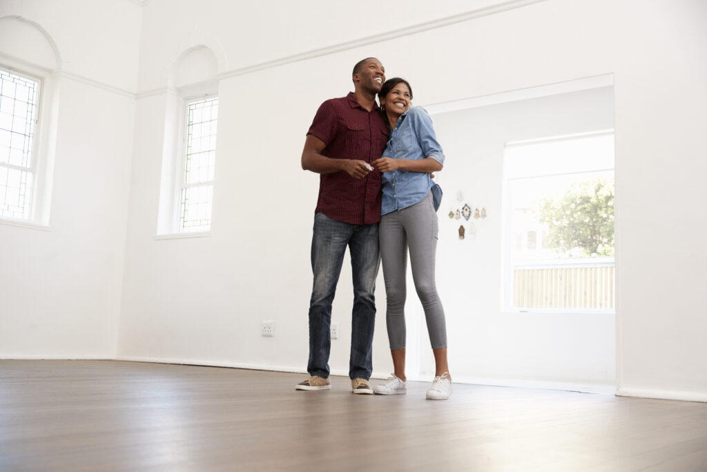 A couple stands together smiling in an empty room while touring a potential rental home.