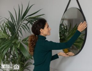 A woman is hanging a mirror on the wall, carefully positioning it for a perfect fit.
