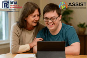 Smiling woman and young adult with Down syndrome sit together at a table using a tablet, representing the mission of ASSIST Disability Services and RPM Regions’ support for inclusive community programs.
