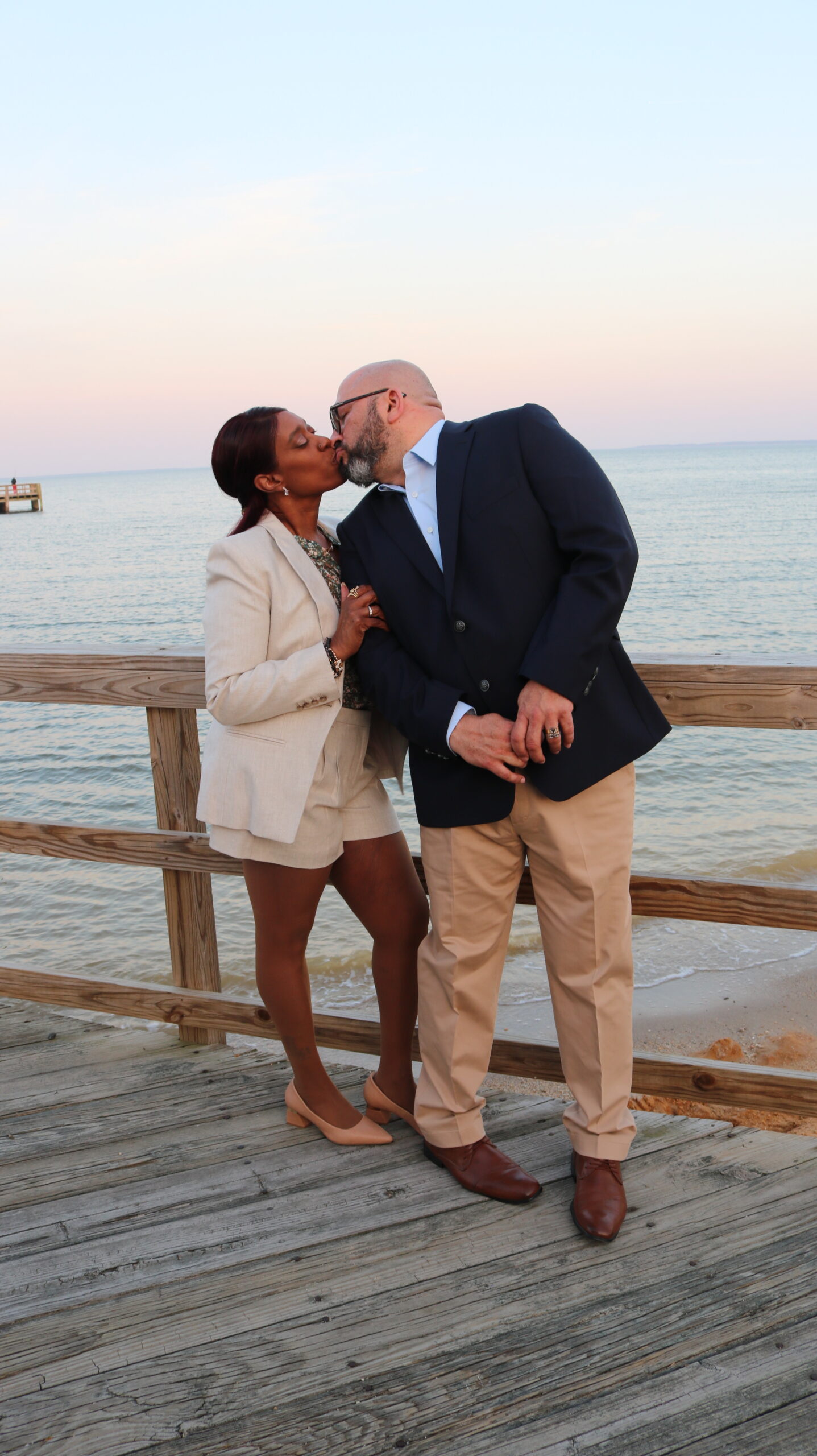 Stephen and Phyllis Guasp sharing a kiss on a waterfront pier at sunset representing love and legacy.