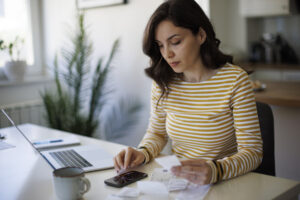A woman sitting at a desk, working on a laptop and surrounded by papers.