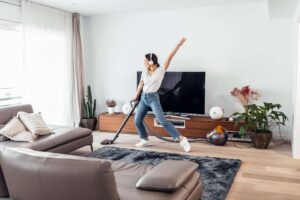Woman listening and dancing to music while cleaning the living room.