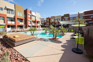 Outdoor pool and patio area at an apartment complex, featuring lounge chairs and greenery for relaxation.