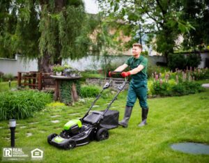 A man in overalls is actively mowing the lawn, surrounded by fresh greenery.