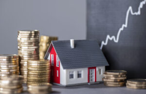 Small model home among stacks of coins and minimalist growth chart behind off to the side. 