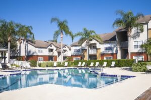 Swimming pool at a condominium complex. Palm trees, chaise lounge, clear sky.