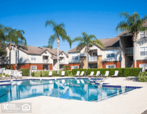 Swimming pool at a condominium complex. Palm trees, chaise lounge, clear sky.