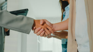 Close-up of Asian female real estate agent handshaking after complete agreement with tenants after showing new houses. Landlord selling real estate to happy couple customer for investment.