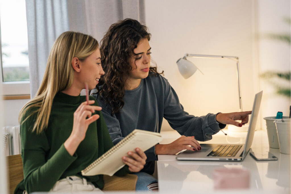 Two roommates at a table, using a laptop to explore renters insurance options together. 
