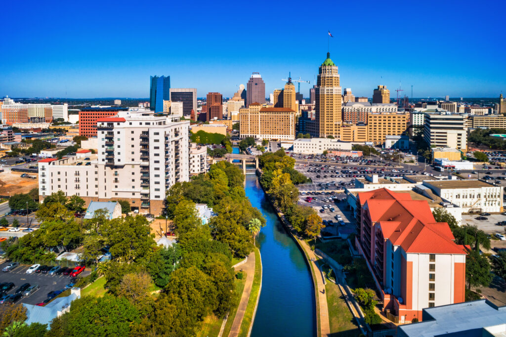 Aerial view of San Antonio's downtown skyline with the Riverwalk and lush trees in the foreground.