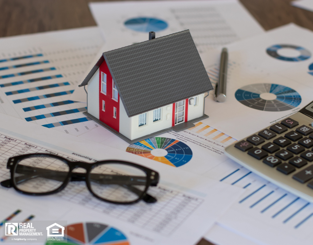 A house model, calculator, glasses, and property tax papers arranged on a desk.