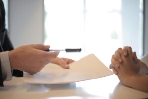 person holding pen and paper and person with their hands crossed