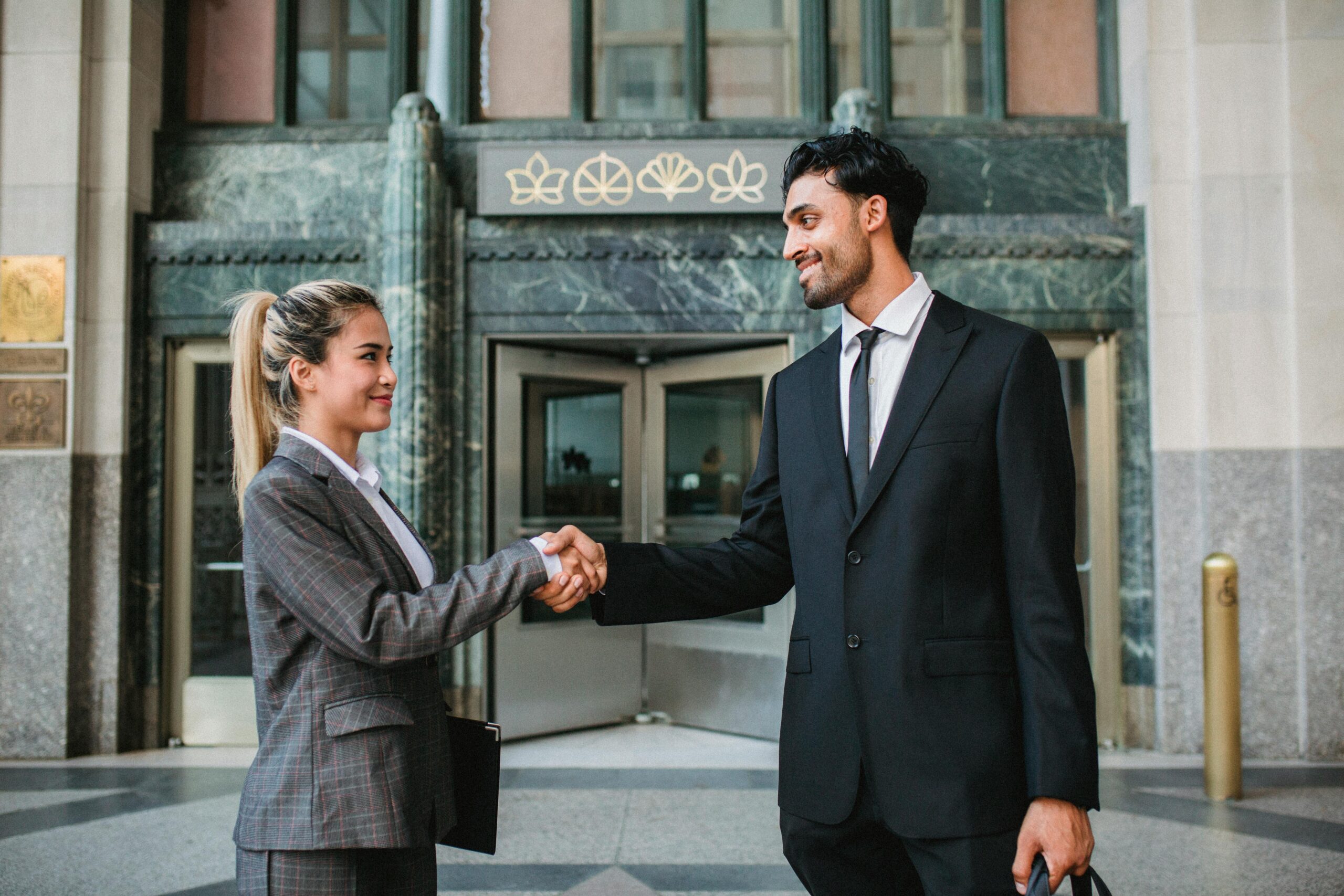 Two people in suits shaking hands outside a bank.