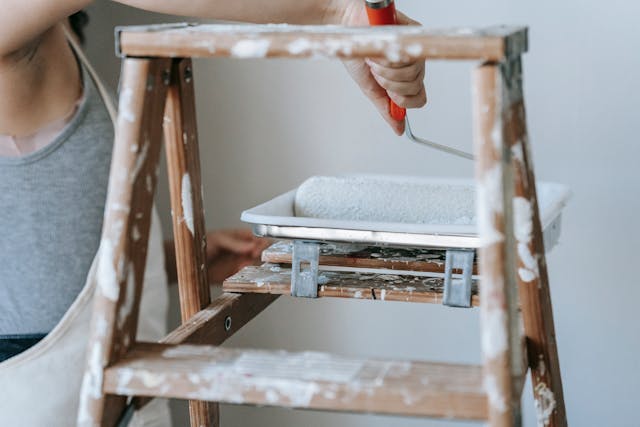 Person dipping a paint roller in a paint tray that is secured to a ladder