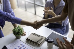 Group of people sitting around a table shaking hands after completing a real estate purchase.
