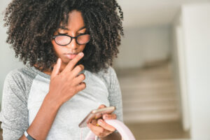 A young woman wearing glasses intently looking at her phone.