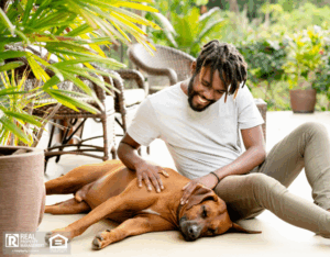 A man sitting on the ground in his backyard, playing with his dog.