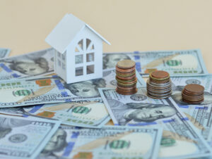 Small model house among American dollars and coins. Home expenses or investing concept. 