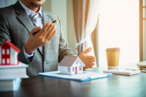 Real estate agent at a desk selling a house with a pen and small model house on clipboard of papers 