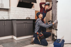 Two mechanics checking refrigerator with screwdriver. 