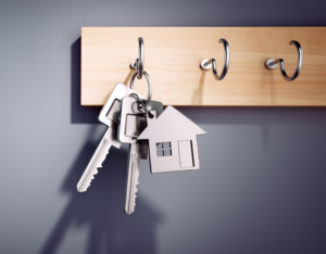 A key ring displaying two keys and a house keychain, hanging from a wall-mounted hook.
