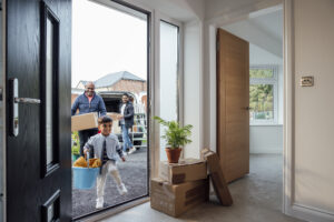 Family moving into a new home unpacking boxes as child excitedly runs through front door. 