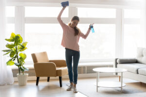 Woman in casual clothes dances while doing house cleaning 