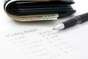 A wallet containing cash positioned next to a pen on a piece of paper, representing budgeting.
