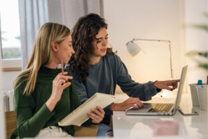 Two roommates at a table, using a laptop to explore renters insurance options together.
