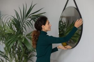 A woman is hanging a mirror on the wall, carefully positioning it for a perfect fit.